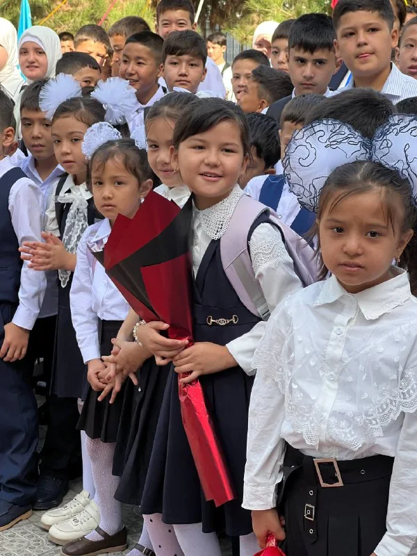 Maktab formasidagi kichik oʻquvchilar birinchi qoʻngʻiroq kuni gul ushlab turibdi